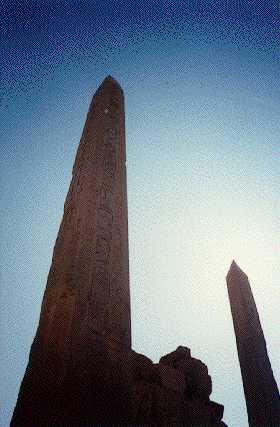 {Two obelisks at Karnak, 
sun hidden behind furthest, making halo around tip}